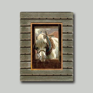 May include: A framed print of a white horse wearing a harness, peeking out of a wooden window. The frame is made of weathered, gray-green wood. The horse's head and upper body are visible, set against a backdrop of a red-roofed building and cloudy sky.