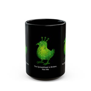 May include: A black ceramic mug featuring a green, digital-style bird graphic composed of various numbers and symbols. Below the bird, the text reads, "The Spreadsheet is Broken, Not Me." The design is printed on the front of the cylindrical mug.
