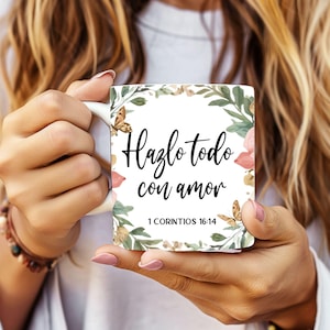 Peut inclure: Tasse en céramique blanche avec l'inscription espagnole « Hazlo todo con amor » (Faites tout avec amour). La tasse est ornée de motifs floraux et de papillons, et contient le verset biblique 1 Corinthiens 16:14.