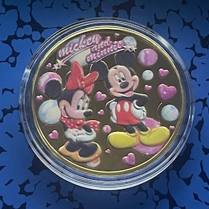 May include: A gold-colored coin with a picture of Mickey Mouse and Minnie Mouse. The coin has the words "mickey and minnie" written on it.
