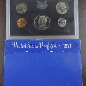 May include: A 1971 United States Proof Set in a clear plastic case, containing five coins. The set includes a penny, nickel, dime, quarter, and half-dollar. The blue packaging reads "United States Proof Set • 1971".