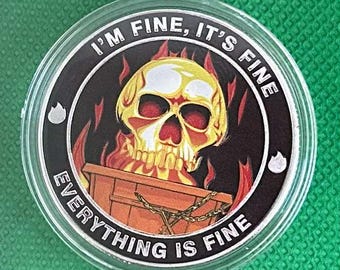 May include: A round, silver-rimmed coin with the phrase "I'M FINE, IT'S FINE" and "EVERYTHING IS FINE" encircling a central image. The image features a yellow skull with red eyes above a wooden coffin engulfed in flames.