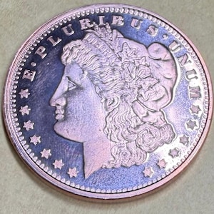May include: A circular silver-toned coin featuring a profile portrait of a figure wearing a cap with the word LIBERTY inscribed. The text E PLURIBUS UNUM is arched along the top edge, surrounded by a series of stars along the coin's perimeter.