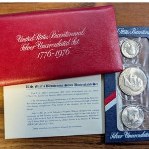 May include: A red leatherette case and a blue and white coin holder containing silver coins. The case is embossed with "United States Bicentennial Silver Uncirculated Set 1776-1976". A printed insert details the coins' specifications.