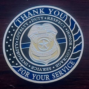 May include: A silver and blue police challenge coin with the words "Thank You For Your Service" and "Integrity, Loyalty, Duty, Respect, Honor, Courage, Service" around the edge. The center of the coin features a silver police badge with the words "Police Officer".