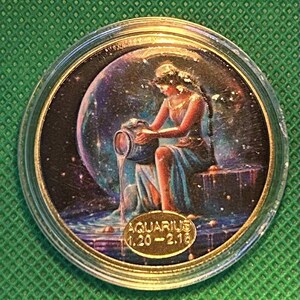 May include: A round coin featuring the Aquarius zodiac sign. The coin depicts a woman pouring water from a jug, set against a starry background. The text "AQUARIUS 1.20-2.18" is displayed on the coin.
