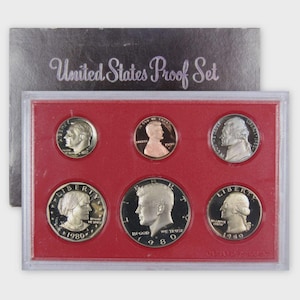 May include: A 1980 United States Proof Set in a clear plastic case with a red insert. The set includes six coins, each with a portrait of a historical figure. The packaging reads "United States Proof Set".