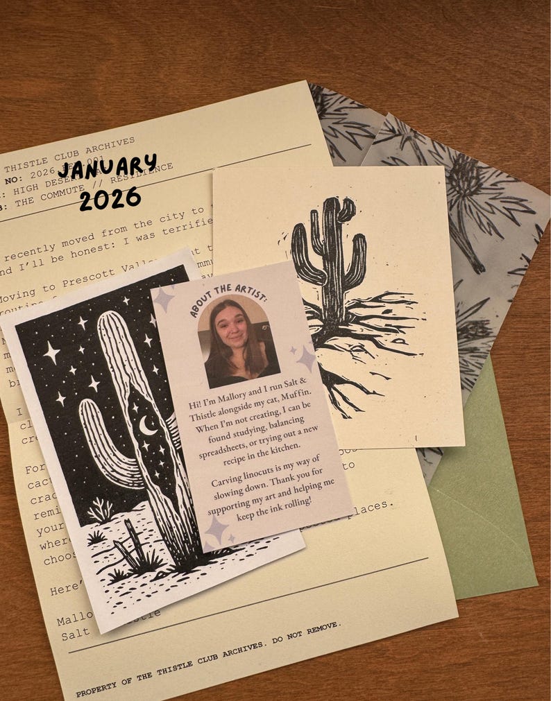 May include: A collection of stationery items featuring cactus illustrations and the text "January 2026". Includes a card with artist information and a linocut print of a cactus. The items are on a wooden surface.