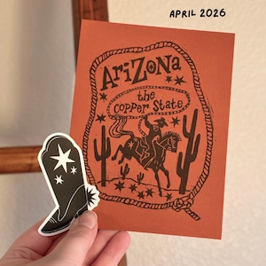 May include: An orange card with the text "Arizona the Copper State" and a cowboy riding a horse illustration. A black and white sticker of a cowboy boot is next to the card. The text "April 2026" is at the top.
