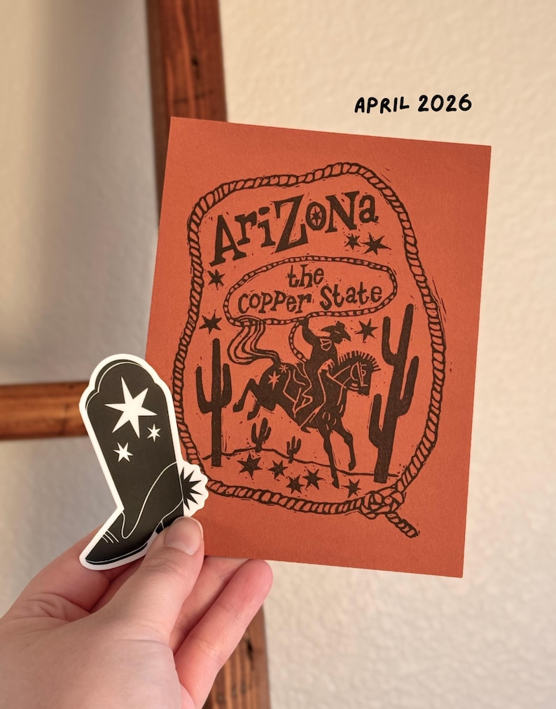 May include: An orange card with the text "Arizona the Copper State" and a cowboy riding a horse illustration. A black and white sticker of a cowboy boot is next to the card. The text "April 2026" is at the top.