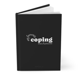 May include: A black hardcover journal with white text on the front cover that reads my favourite coping mechanism. The book is slightly open, revealing white pages inside. The cover has a matte finish and a clean, vertical spine design.