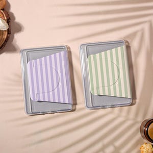 May include: Two clear plastic cardholders, each containing a card with a striped design. One card is lavender with white stripes, the other is green with white stripes. The cardholders are on a light pink surface.