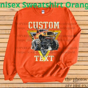 May include: Orange unisex sweatshirt featuring a monster truck graphic. The design includes the word "CUSTOM" above the truck and "TEXT" below, set against a yellow and black triangle. The sweatshirt has long sleeves and a crew neck.