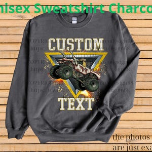 May include: Charcoal grey unisex sweatshirt with a monster truck graphic. The design includes the words "CUSTOM" and "TEXT" in a bold font, and a monster truck graphic inside a yellow triangle. The text "Unisex Sweatshirt Charcoal" is at the top.