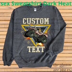 May include: Dark heather grey unisex sweatshirt with a custom design. The design features a monster truck graphic inside a yellow triangle, with the words "CUSTOM" and "TEXT". The sweatshirt is a comfortable, casual style.