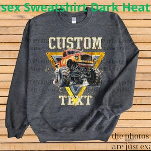 May include: Dark heather gray unisex sweatshirt featuring a custom design. The design includes a monster truck illustration within a yellow triangle, with the words "CUSTOM" and "TEXT" above and below the truck. The sweatshirt is a comfortable, casual style.