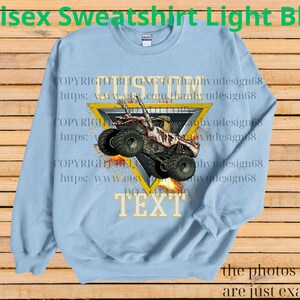 May include: Pale blue unisex sweatshirt featuring a monster truck graphic within a yellow triangle. The text "CUSTOM TEXT" is below the triangle. The words "Unisex Sweatshirt Light Blue" are at the top of the sweatshirt.