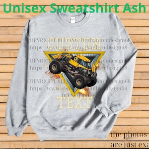K&ouml;nnte beinhalten: Hellgraues Unisex-Sweatshirt mit einem gelben Monster-Truck-Design in einem gelben Dreieck. Das Sweatshirt hat den Text "TEXT" in goldenen Buchstaben. Die Worte "Unisex Sweatshirt Ash" stehen oben auf dem Sweatshirt.