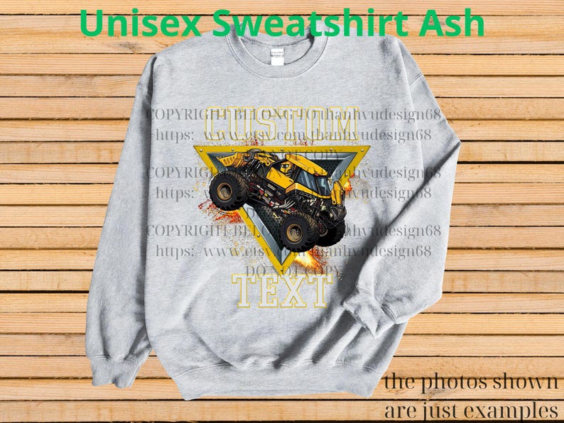 K&ouml;nnte beinhalten: Hellgraues Unisex-Sweatshirt mit einem gelben Monster-Truck-Design in einem gelben Dreieck. Das Sweatshirt hat den Text "TEXT" in goldenen Buchstaben. Die Worte "Unisex Sweatshirt Ash" stehen oben auf dem Sweatshirt.