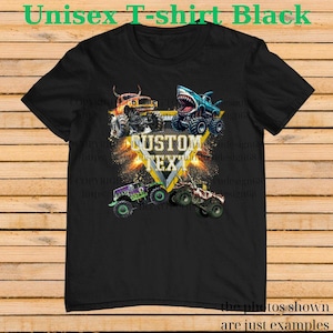 May include: Black unisex t-shirt featuring a graphic of four monster trucks in vibrant colors. The design includes a shark-themed truck and the words "CUSTOM TEXT" in a yellow triangle. The shirt's text reads "Unisex T-shirt Black".