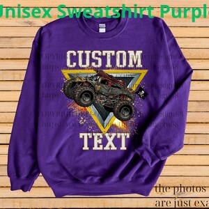 May include: A purple unisex sweatshirt featuring a custom design. The design includes a monster truck graphic within a yellow triangle, with the words "CUSTOM TEXT" in white block letters. The sweatshirt has long sleeves.