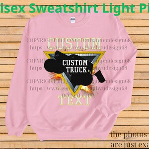 May include: Pale pink unisex sweatshirt featuring a black custom truck graphic within a yellow triangle. The words "CUSTOM TRUCK" are on the graphic. The sweatshirt also has the text "TEXT" at the bottom.
