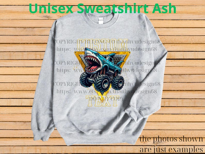 May include: Ash gray unisex sweatshirt featuring a cartoon shark monster truck design. The shark truck is blue with a yellow triangle background. The text "DO NOT COPY TEXT" is visible. The words "Unisex Sweatshirt Ash" are at the top.