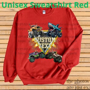 May include: Red unisex sweatshirt featuring a graphic of monster trucks with the text "CUSTOM TEXT". The sweatshirt has a crew neck and long sleeves. The text "Unisex Sweatshirt Red" is at the top.