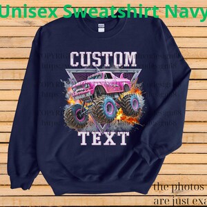 Op de afbeelding: Marineblauwe unisex sweatshirt met een roze monstertruck ontwerp en de woorden "CUSTOM TEXT". De truck heeft grote banden en staat tegen een achtergrond van vlammen en een driehoek. De tekst "Unisex Sweatshirt Navy" staat bovenaan.