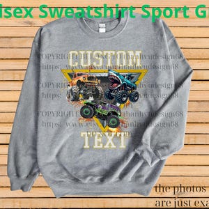 May include: Sport grey unisex sweatshirt featuring a graphic of three monster trucks in orange, blue, and green, with the words "CUSTOM TEXT" in a yellow triangle. The sweatshirt has long sleeves and a crew neck.