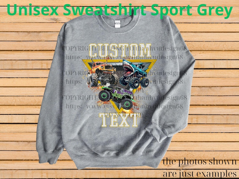 May include: Sport grey unisex sweatshirt featuring a graphic of three monster trucks in orange, blue, and green, with the words "CUSTOM TEXT" in a yellow triangle. The sweatshirt has long sleeves and a crew neck.