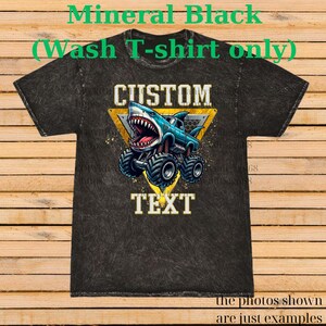 May include: Black mineral wash t-shirt with a graphic of a shark-themed monster truck. The design includes the words "CUSTOM" and "TEXT" in a yellow triangle. The shirt is a dark gray color.