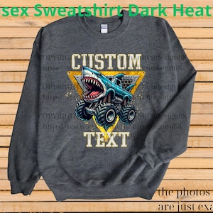 May include: Dark heather gray unisex sweatshirt featuring a cartoon monster truck with a shark head. The design includes the words "CUSTOM" and "TEXT" in a yellow triangle. The sweatshirt is a comfortable, casual style.