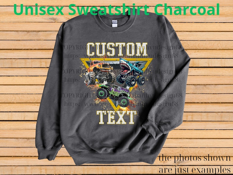May include: Charcoal gray unisex sweatshirt featuring a graphic of three monster trucks in orange, blue, and green. The design includes the text "CUSTOM TEXT" within a yellow triangle. The sweatshirt has a crew neck.