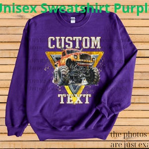 May include: Purple unisex sweatshirt featuring a custom design of an orange monster truck within a yellow triangle, with the words "CUSTOM" and "TEXT". The sweatshirt has long sleeves and a crew neck.