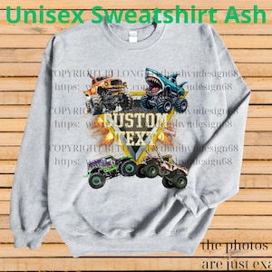 May include: Ash gray unisex sweatshirt featuring a design of four monster trucks with flames and the text "CUSTOM TEXT". The sweatshirt also has the text "Unisex Sweatshirt Ash" at the top and "the photos shown are just examples" at the bottom.