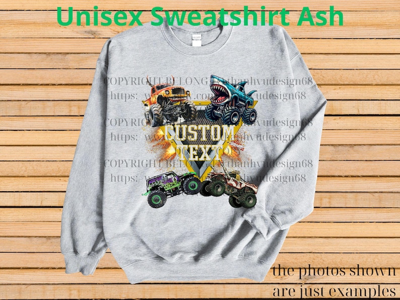 May include: Ash gray unisex sweatshirt featuring a design of four monster trucks with flames and the text "CUSTOM TEXT". The sweatshirt also has the text "Unisex Sweatshirt Ash" at the top and "the photos shown are just examples" at the bottom.