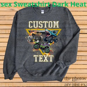 May include: Dark heather gray unisex sweatshirt with a graphic of three monster trucks. The design includes the words "CUSTOM TEXT" in a yellow triangle. The sweatshirt is a crew neck style.