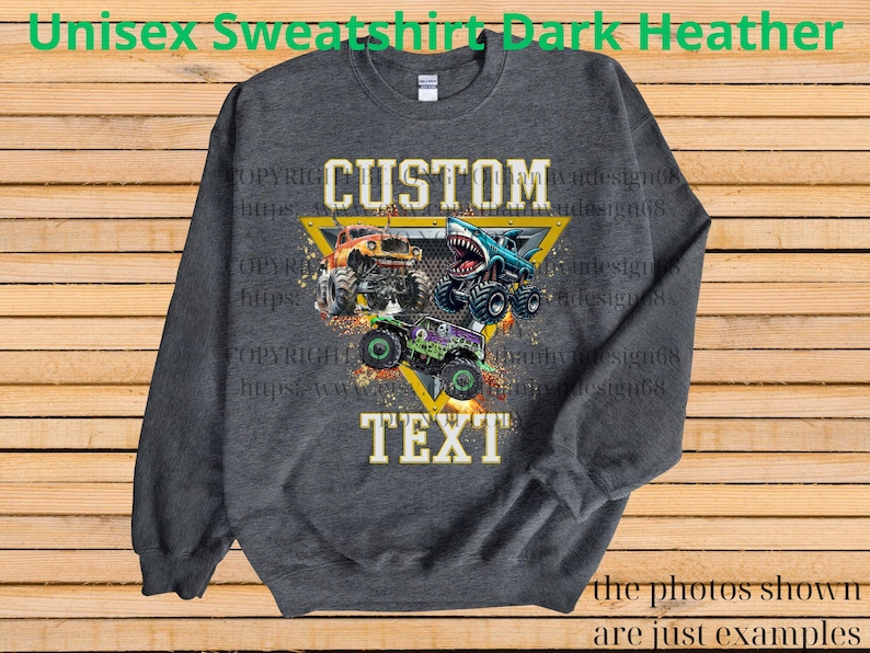 May include: Dark heather gray unisex sweatshirt with a graphic of three monster trucks. The design includes the words "CUSTOM TEXT" in a yellow triangle. The sweatshirt is a crew neck style.