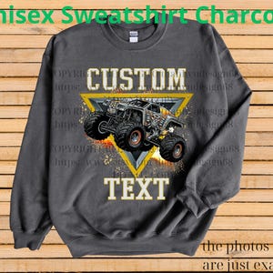 May include: Charcoal grey unisex sweatshirt with a custom monster truck design. The design features a monster truck inside a yellow triangle with the word "CUSTOM" above and "TEXT" below. The text "Unisex Sweatshirt Charcoal" is at the top.