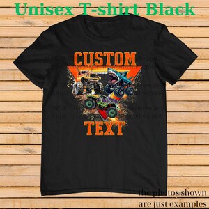 以下が含まれることがあります： 黒色のユニセックスTシャツ。3台のモンスタートラックのグラフィックと、オレンジ色の「CUSTOM TEXT」の文字が特徴です。トラックは黄色、青、緑の色合いです。Tシャツには「Unisex T-shirt Black」の文字も入っています。