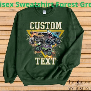 May include: Forest green unisex sweatshirt with a graphic of three monster trucks in orange, blue, and green. The design includes the words "CUSTOM" and "TEXT" in white, set within a yellow triangle. The text "Unisex Sweatshirt Forest Green" is at the top.