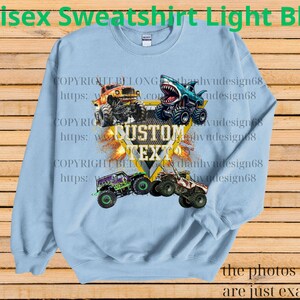 May include: Light blue unisex sweatshirt featuring a graphic of monster trucks with the text "CUSTOM TEXT". The sweatshirt has a crew neck and long sleeves. The words "Unisex Sweatshirt Light Blue" are at the top.