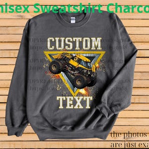 K&ouml;nnte beinhalten: Anthrazitgraues Unisex-Sweatshirt mit individuellem Design. Das Design zeigt einen gelben Monstertruck in einem gelben Dreieck mit dem Wort "CUSTOM" oben und "TEXT" unten. Der Text "Unisex Sweatshirt Charcoal" steht oben.