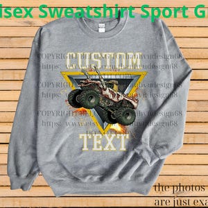 May include: A grey unisex sweatshirt featuring a monster truck design within a yellow triangle. The words "CUSTOM" and "TEXT" are displayed above and below the truck graphic. The text "Unisex Sweatshirt Sport Grey" is at the top.