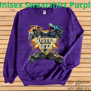 May include: A purple unisex sweatshirt featuring a graphic of monster trucks. The design includes a shark-themed truck and the text "CUSTOM TEXT" in a yellow and white design. The text "Unisex Sweatshirt Purple" is at the top.