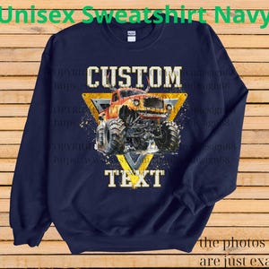 May include: Navy blue unisex sweatshirt with a graphic of a monster truck inside a yellow triangle. The words "CUSTOM" and "TEXT" are above and below the truck. The sweatshirt has the text "Unisex Sweatshirt Navy" at the top.