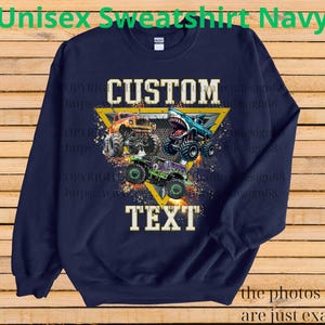 May include: Navy blue sweatshirt with a graphic of three monster trucks in orange, blue, and green. The design includes the words "CUSTOM" and "TEXT" in a yellow triangle. The text "Unisex Sweatshirt Navy" is at the top.