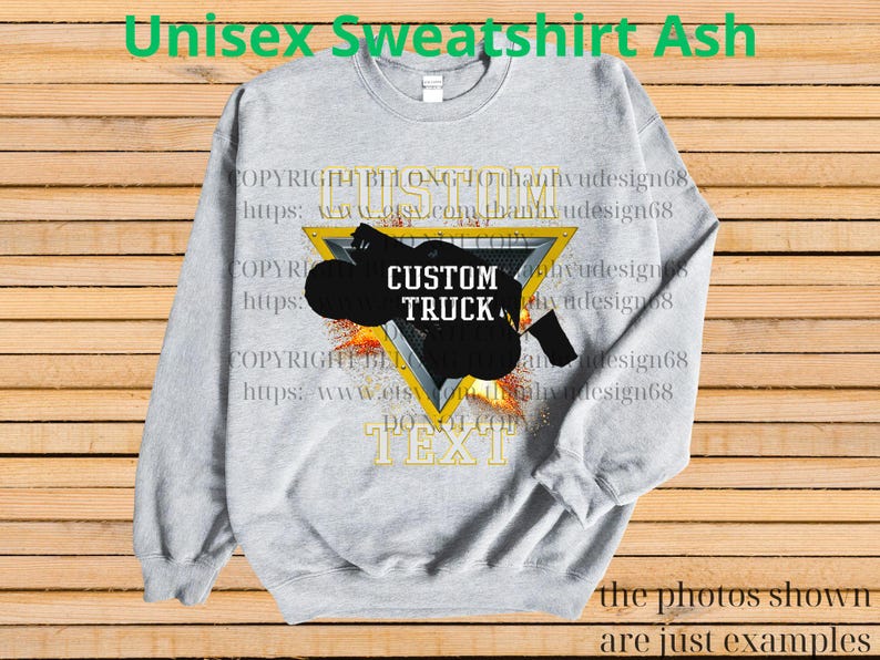 May include: Grey unisex sweatshirt with a black custom truck design inside a yellow triangle. The sweatshirt has the text "CUSTOM TRUCK" and other text. The background is a wooden surface.