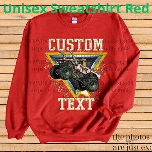 May include: A red unisex sweatshirt featuring a monster truck graphic within a yellow and grey triangle. The words "CUSTOM" and "TEXT" are displayed above and below the truck image. The text "Unisex Sweatshirt Red" is at the top.